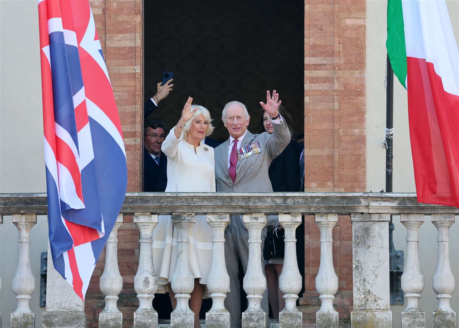 The King and Queen wave from a balcony during a visit to a UK-Emilia Romagna Food Festival at Piazza del Popolo, in the heart of Ravenna (Chris Jackson/PA)