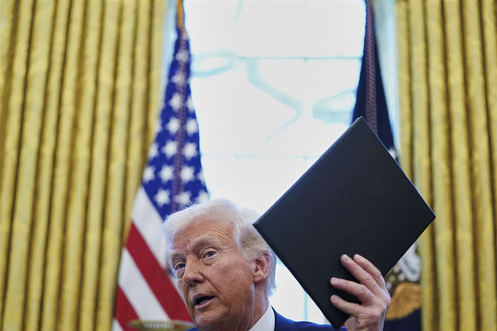 President Donald Trump holds an executive order in the Oval Office of the White House in Washington (Pool via AP)
