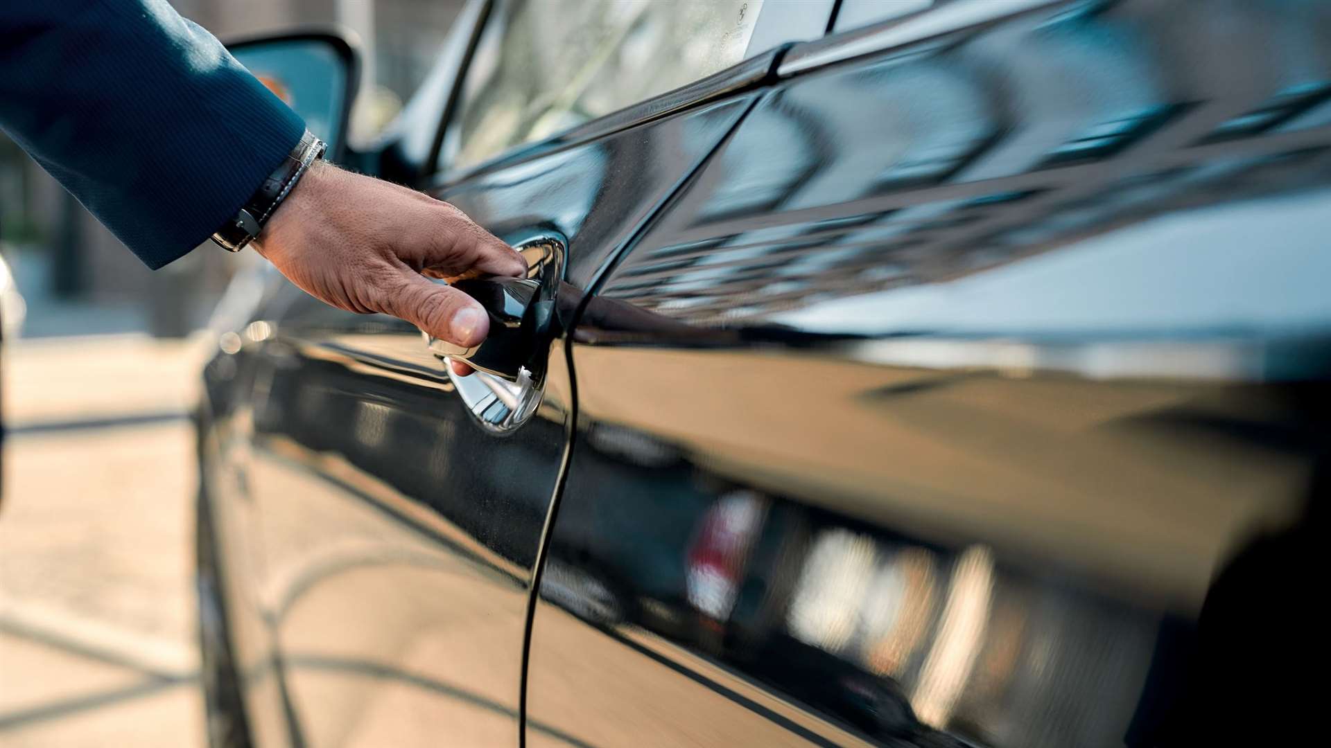 Cropped photo of a male hand opening the door of a black car while standing outdoors. Close up. Transportation limo chauffeur credit: istock/LanaStock