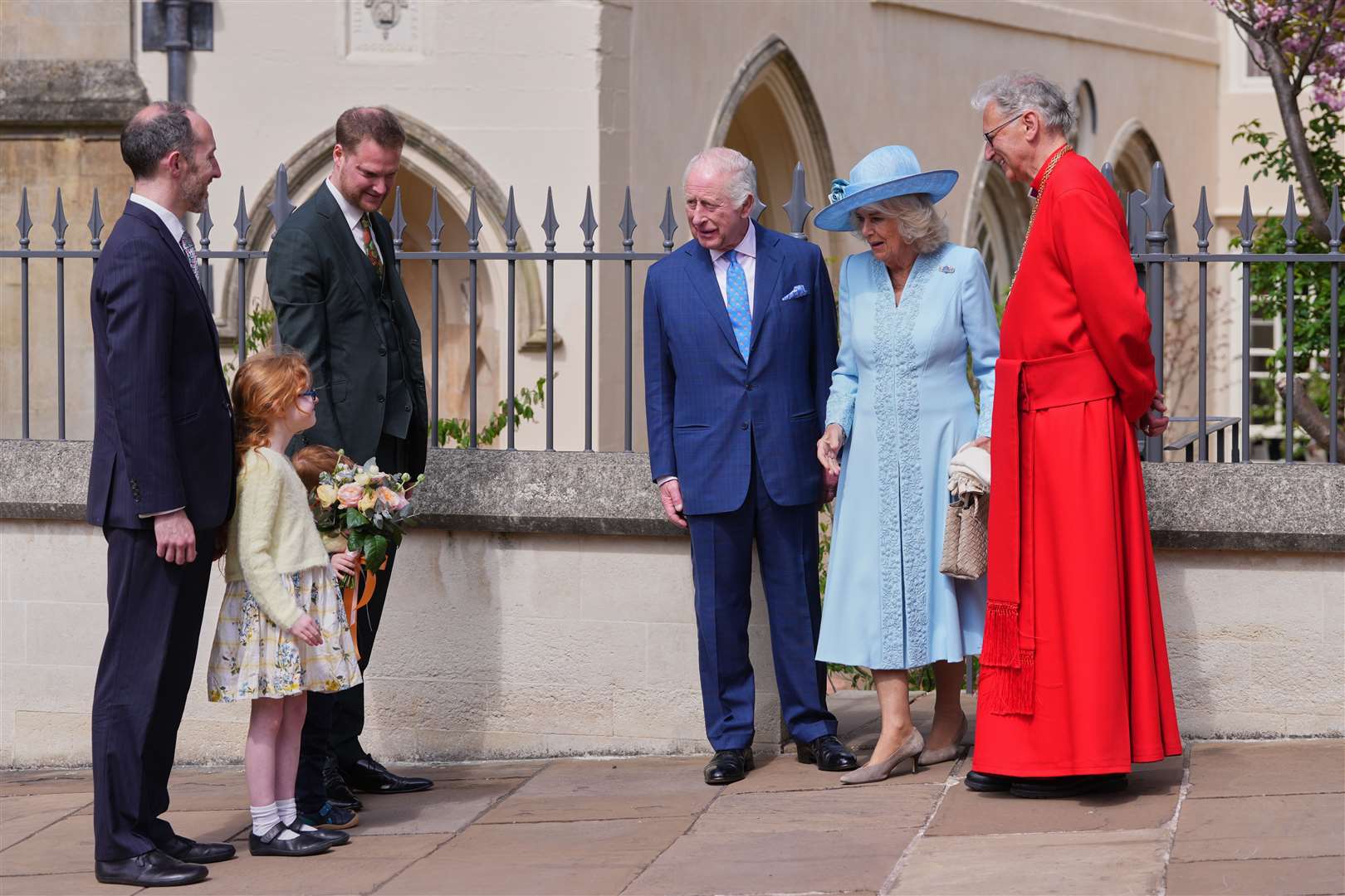 The Dean of Windsor, the Right Rev Christopher Cocksworth, stands with the King and Queen Camilla, as they look at a young girl who will present a posy (Kirsty Wigglesworth/PA)